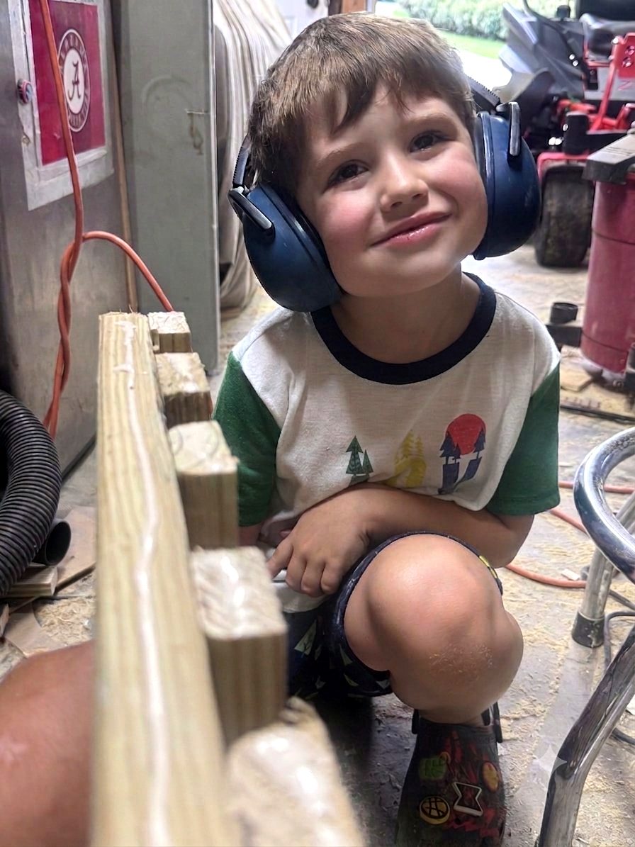 Sawyer in the workshop with hearing protection on helping build a wooden viewing platform for the beehives